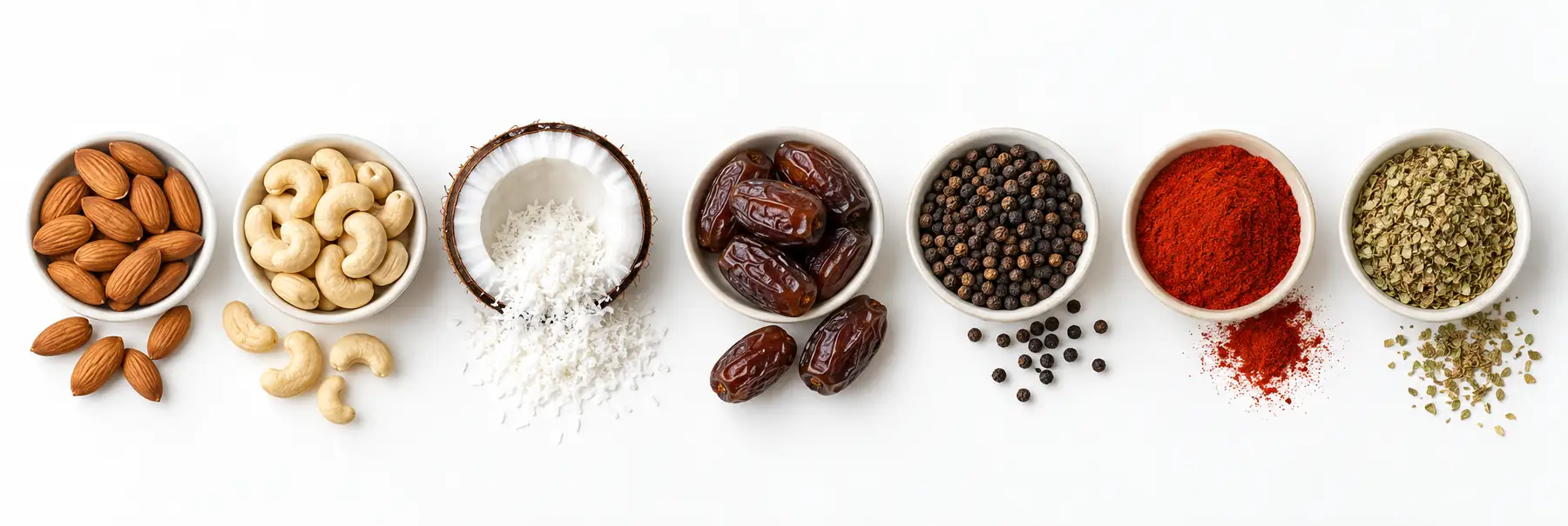Seven of our products seen from above: almonds, cashew nuts, coconut, dates, black pepper, paprika and oregano